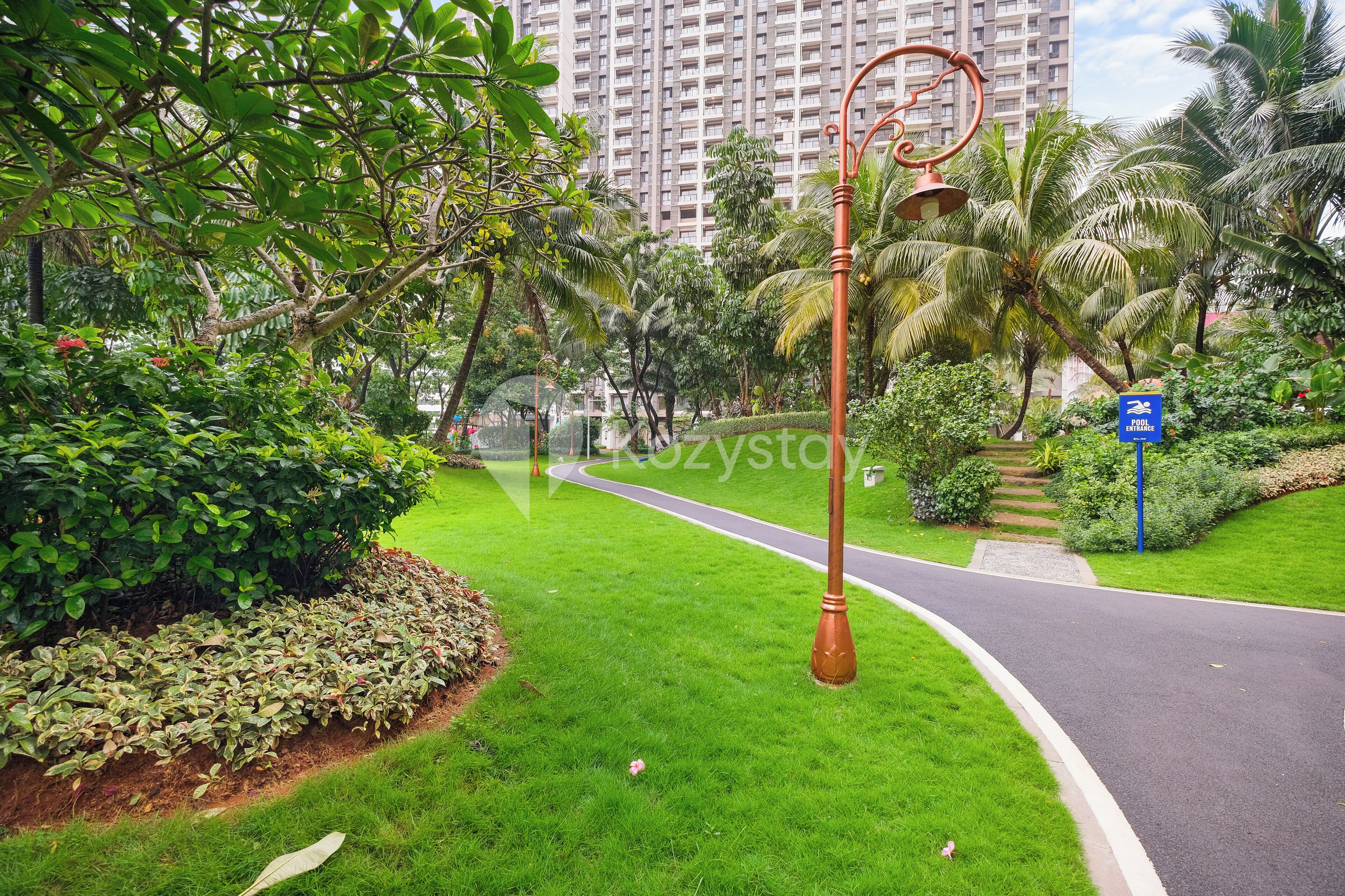 Un jardín bien cuidado con un sendero curvo, una farola y un letrero azul que indica una zona peatonal.