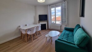 A compact living space with a dining table, a sofa, a television, and a window with a view.