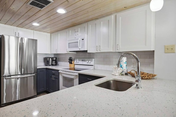 A modern kitchen with stainless steel appliances, white cabinetry, and a speckled countertop.