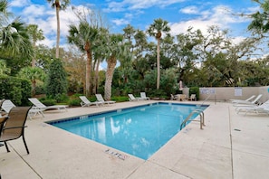 Piscina com espreguiçadeiras e palmeiras ao fundo.
