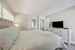 A bedroom with a bed, a dresser, a television, and a mirror.