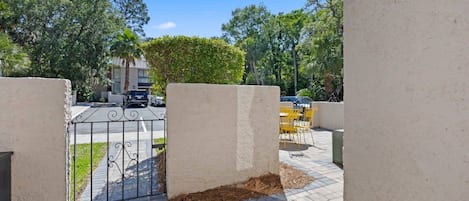 A gated entrance with a paved pathway leading to a seating area with yellow chairs.