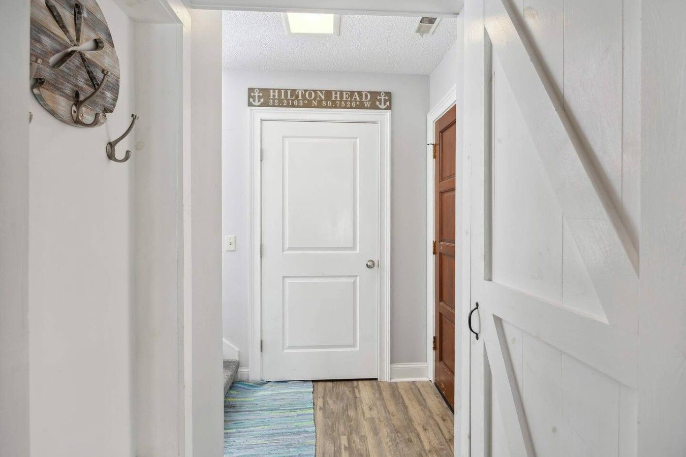 Um corredor com uma porta branca, piso de madeira e uma placa sobre a porta.