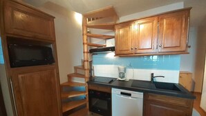 Une cuisine compacte dotée de meubles en bois, d’un four encastré, d’un lave-vaisselle et d’un petit plan de travail avec un évier.
