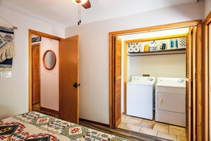 A room with a bed, a wooden door, a mirror, a closet with a washing machine, and a patterned rug. - Pine Acres Velo (Durango)