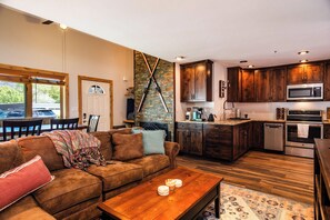 A modern kitchen with dark wooden cabinets, stainless steel appliances, and a brick accent wall. - Pine Acres Velo (Durango)