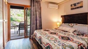A bedroom with a bed, a ceiling fan, an air conditioning unit, a window with curtains, and a view of the outdoors.