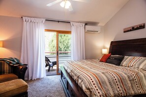 Un dormitorio con una cama grande, cabecera de madera, una banca, una silla y vistas al exterior a través de una puerta corredera.