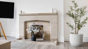 A fireplace with a vase of flowers, a potted plant, and a flat-screen TV mounted on the wall.