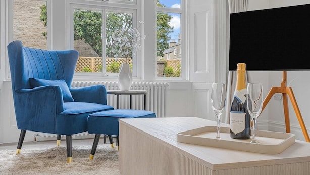 A room with a blue armchair, a small table with a bottle of champagne, glasses, and a projector screen.