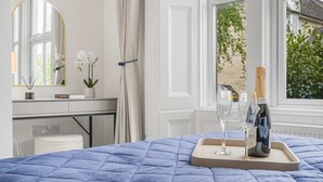 A bedroom with a blue quilted bedspread, a bedside table with a bottle of champagne, two glasses, and a tray.