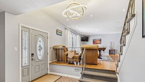 Ein geräumiger Wohnbereich mit Treppe, einer großen Kronleuchter und einem an der Wand befestigten Fernseher.