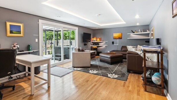 Ein modernes Wohnzimmer mit einem weißen Schreibtisch, einem braunen Sofa und Holzboden. Ein großes Fenster bietet Blick auf Grünflächen.