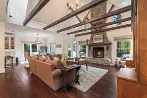 A spacious living room with a stone fireplace, wooden beams, and a large window overlooking greenery. - Grayling Cottage - Walk to Highlands Main Street (Highlands)
