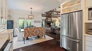 A spacious kitchen with a large stainless steel refrigerator, a dining area with a patterned tablecloth, and a fireplace in the background.