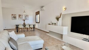 A modern living room with a sectional sofa, a glass coffee table, a flat-screen TV, and a dining area with a table and chairs.