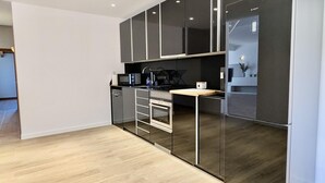 A modern kitchen with dark cabinetry, a stainless steel refrigerator, and a wooden countertop.