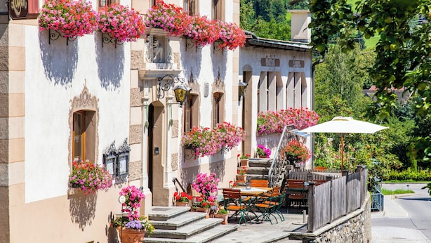 A building with a stone facade, outdoor seating area with tables and chairs, and flower boxes on the windowsills. - Gasthof Löwen by Hotel Montafoner Hof (Tschagguns)