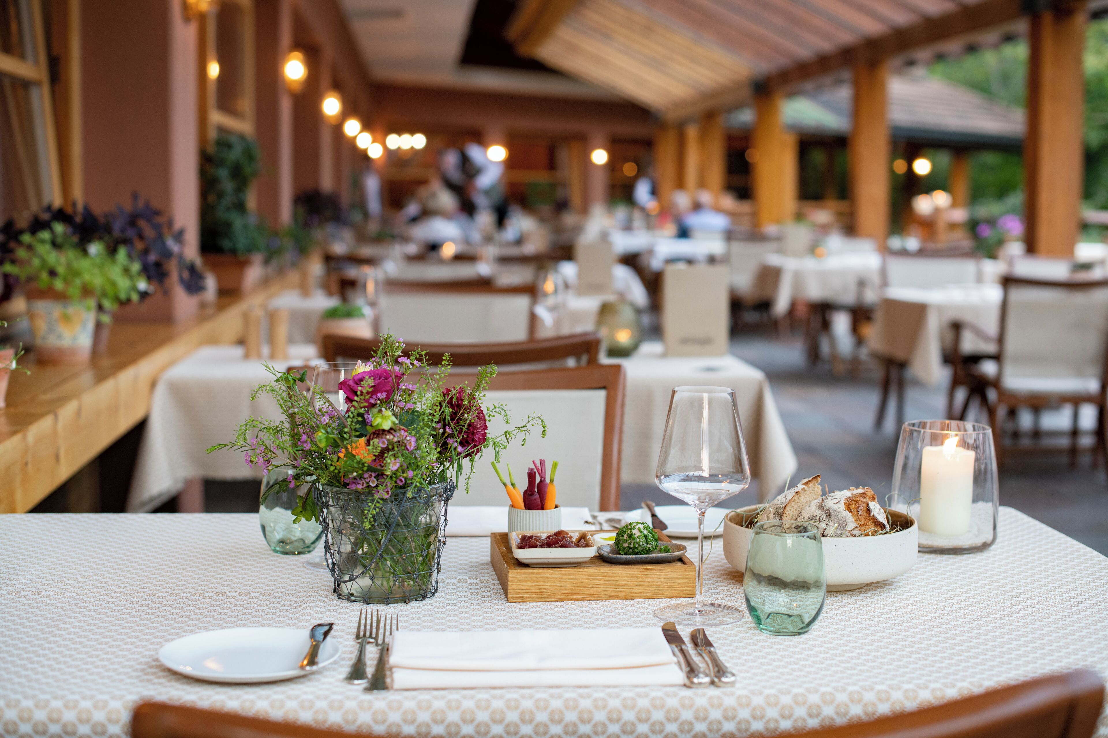 Ein Restaurant mit gedeckten Tischen, einer Blumenvase, einer Kerze und einem Weinglas.