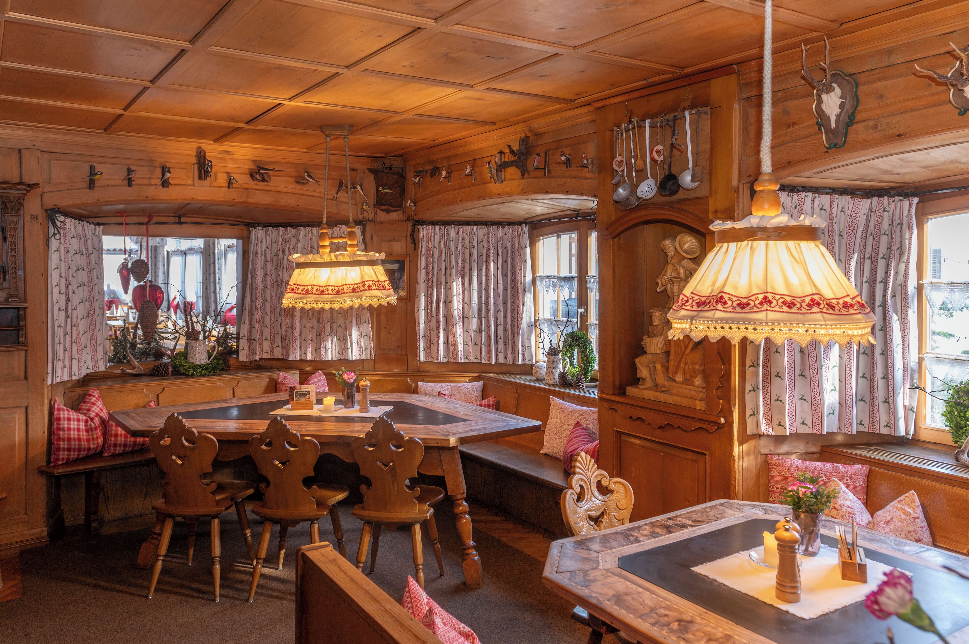 A cozy wooden interior with a large dining table, benches, and hanging lamps.