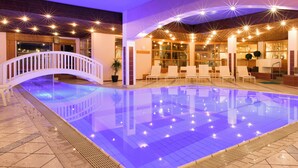 A swimming pool with a white arch bridge, lounge chairs, and a reception area with a large window. - Gasthof Löwen by Hotel Montafoner Hof (Tschagguns)