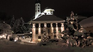 A snow-covered building with a clock tower, illuminated windows, and snow-laden trees. - Gasthof Löwen by Hotel Montafoner Hof (Tschagguns)