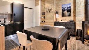 Une cuisine moderne avec des meubles de couleur sombre, un coin repas avec une table et des chaises en bois, et une cheminée.