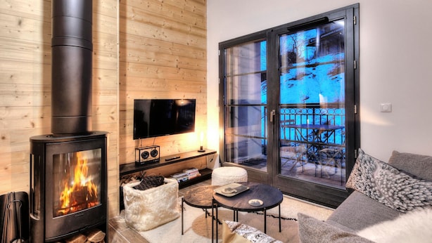 Un salon chaleureux avec un poêle à bois, un téléviseur à écran plat et un coin salon confortable donnant sur une terrasse extérieure enneigée.