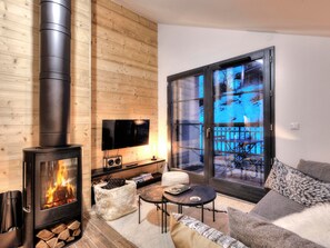 Un salón acogedor con estufa de leña, televisor de pantalla plana y una zona de estar confortable con vistas a una terraza nevada.