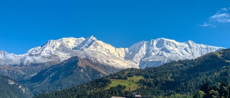 A mountain lodge with a sloped roof, surrounded by forested mountains and a clear blue sky.