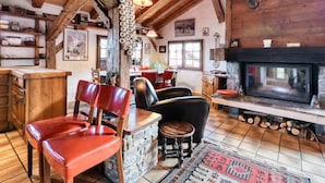Un interior rústico con chimenea de piedra, vigas de madera y un comedor con sillas rojas.