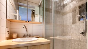 Un baño moderno con ducha acristalada, lavabo con grifo y espejo sobre él.