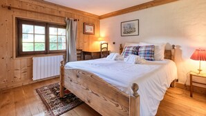 Un dormitorio con paneles de madera, una cama, una ventana, un radiador y una lámpara.