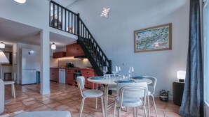 A dining area with a table set for four, a staircase, and a kitchen in the background. - Duplex 83m², 3 bedrooms, 6 pers, central Saint-Gervais, 5 min to cable car, Wifi included (Saint-Gervais-les-Bains)