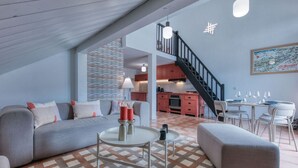 A modern living room with a sofa, ottoman, and coffee table, a staircase leading to a kitchen, and a dining area with chairs and glasses. - Duplex 83m², 3 bedrooms, 6 pers, central Saint-Gervais, 5 min to cable car, Wifi included (Saint-Gervais-les-Bains)
