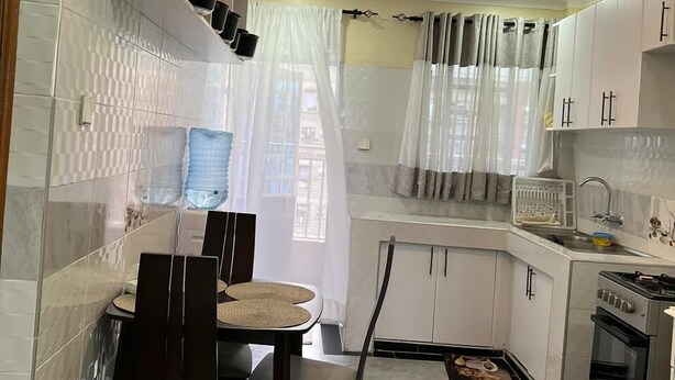 A compact kitchen with white cabinets, a dining table with chairs, a stove, and a sink.