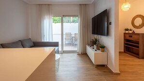 A modern living room with a sofa, a TV mounted on the wall, a wooden cabinet, and a sliding glass door leading to an outdoor area. - The Secret Garden Stay (Agia Paraskevi)