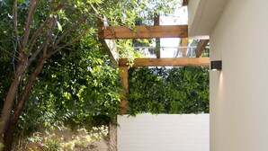 A narrow pathway leading to a white door, flanked by lush greenery and a wooden pergola. - The Secret Garden Stay (Agia Paraskevi)