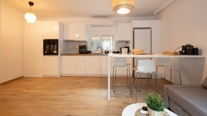 A modern kitchen with white cabinets, a central island, and a hanging light fixture. - The Secret Garden Stay (Agia Paraskevi)