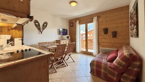 Ein gemütliches Blockhauszimmer mit Holzvertäfelung, einem Essbereich mit Tisch und Stühlen, einer Küchenzeile mit Herd und Spüle sowie einem großen Fenster mit Vorhängen.