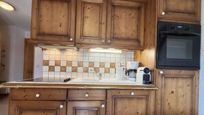 Eine Küche mit Holzausstattung, einer gefliesten Spritzschutzleiste, einer Kaffeemaschine und einem eingebauten Backofen.
