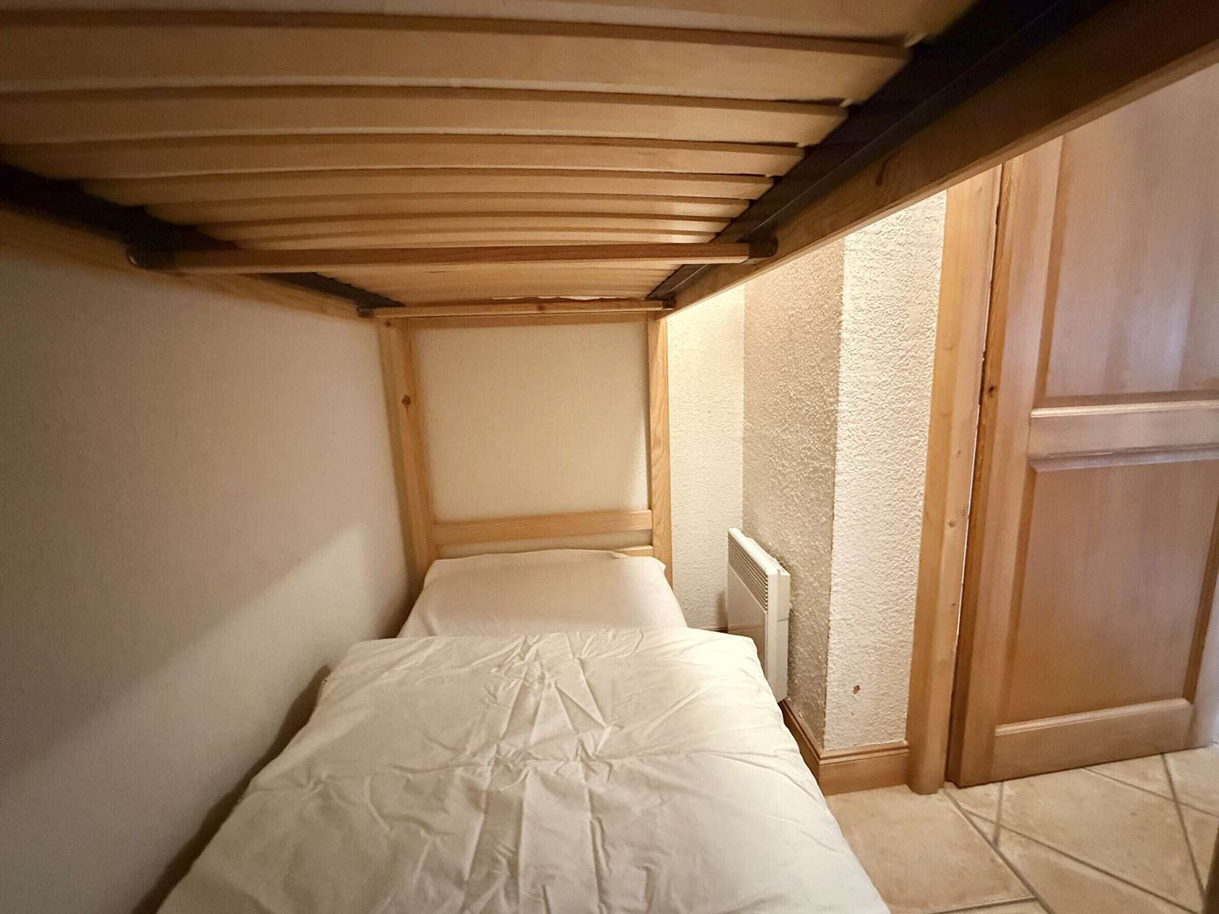 Ein kleines, schmales Schlafzimmer mit Holzbalkendecke und Heizkörper.