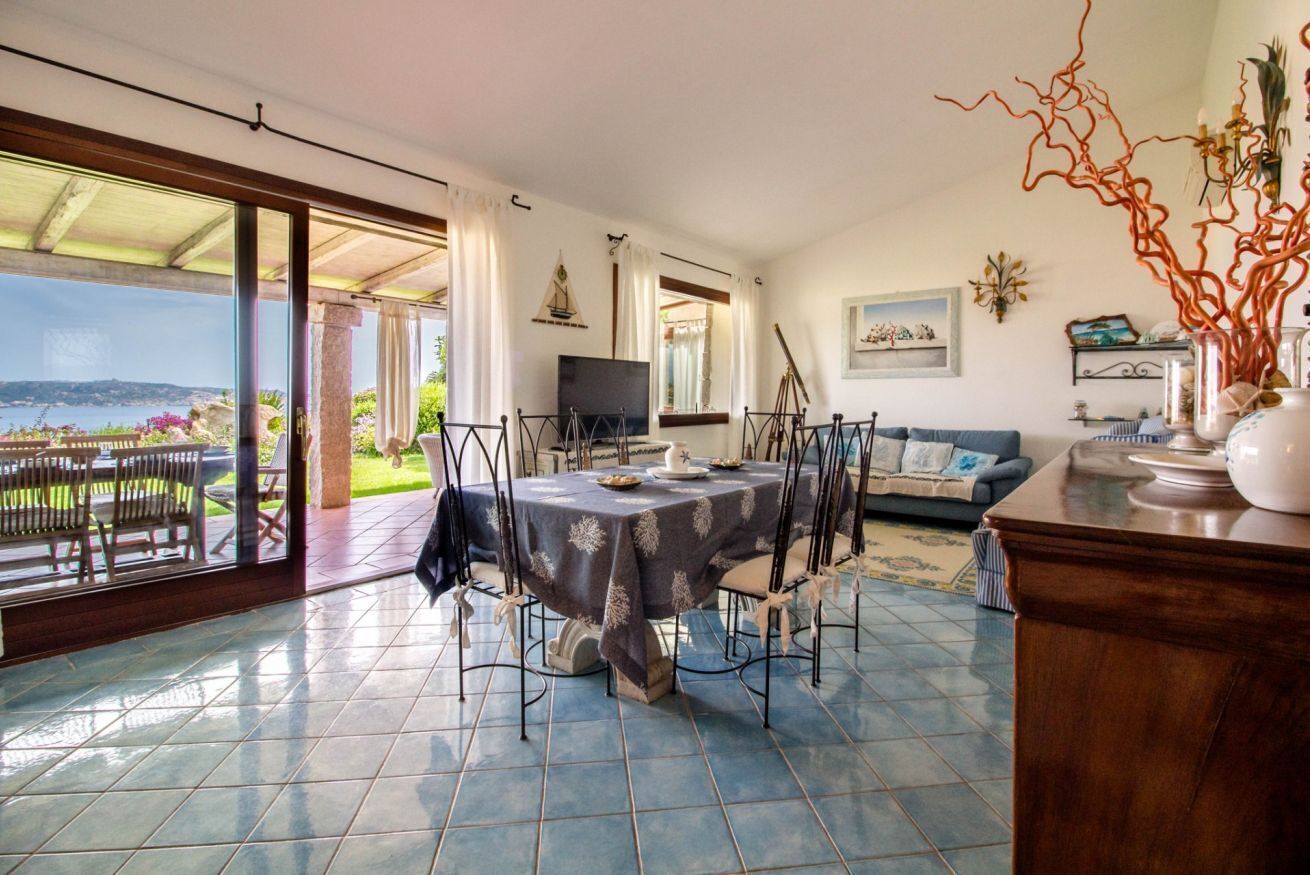 Uma sala de jantar com uma mesa posta para quatro pessoas, um sofá e uma televisão.