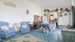 Ein Wohnzimmer mit gestreiften Sofas, einem Esstisch mit Stühlen, einer Küche im Hintergrund und einem gemusterten Teppich.