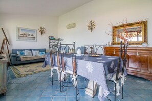 A dining area with a table set for four, a sofa, a mirror, and a framed picture on the wall.