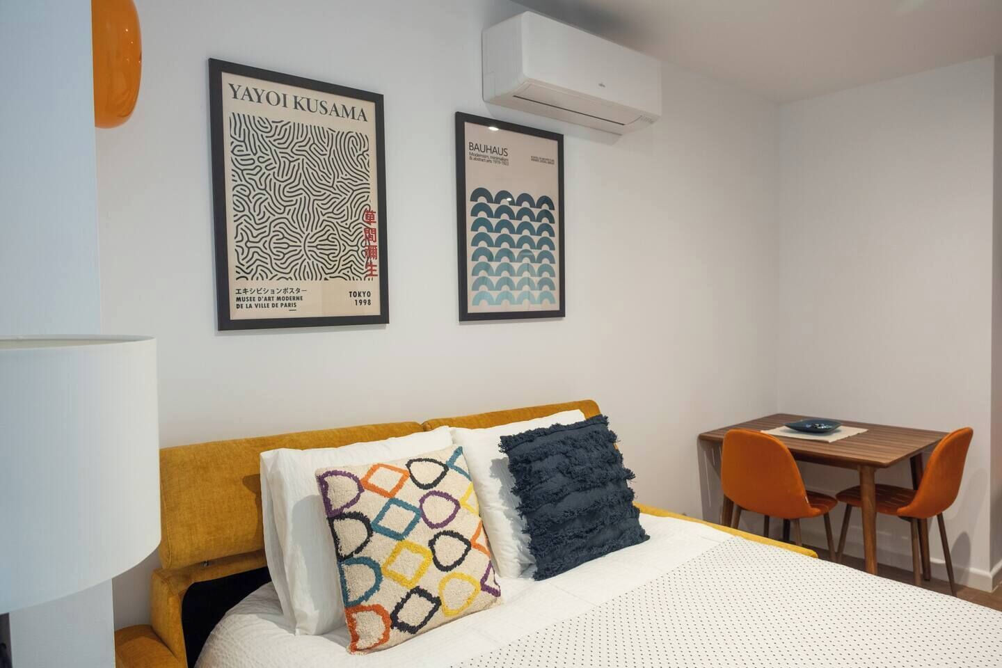 Hotellihuone, jossa on sänky, työpöytä ja kaksi kehystettyä taideteosta seinällä.
