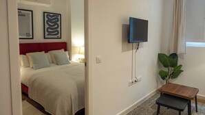 A hotel room with a bed, a TV mounted on the wall, a small table, and a potted plant.