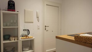A compact kitchen with white cabinetry, a coffee maker, a kettle, and a basket on the counter.