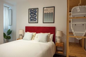 A hotel room with a red headboard, a bed with white bedding, two wall-mounted lamps, and two framed pictures.