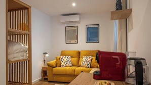 Una sala de estar acogedora con un sofá color mostaza, una estantería de madera y una cafetera roja.